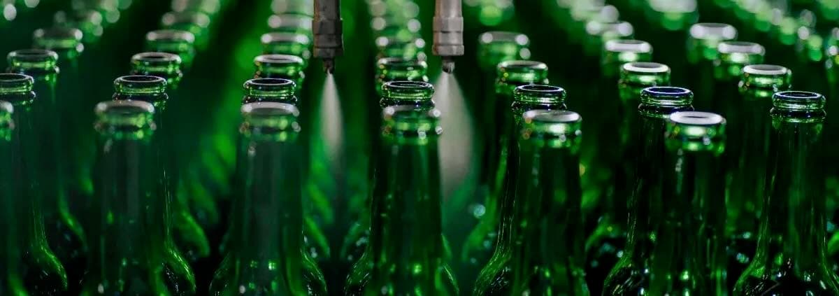 Rows of green glass bottles moving along a bottling production line.